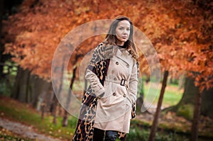 young girl in overcoat in forest. Fashion woman in coat in park. Slim young fashion model wearing white coat outdoor.