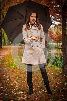 young girl in overcoat in forest. Fashion woman in coat in park. Slim young fashion model wearing white coat outdoor.