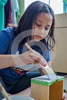 A young girl painting boxes in white colour. Upcycle, recycle and home makeover project