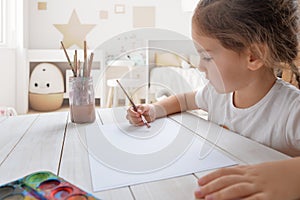 Young girl painting with watercolors on white paper in her room