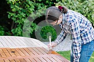 Young girl painting wooden exotic wood table in the garden with a brush - shallow depth of field