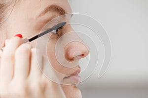 A young girl paints her eyelashes with mascara. Face close-up. facial care photo