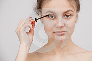 A young girl paints her eyelashes with mascara. Face close-up. facial care photo
