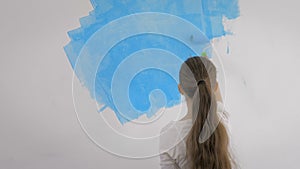 Young girl paints the wallpaper with a roller in the room with blue paint