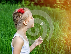 Young girl in the park blowing on dandelion
