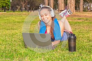 A young girl in a park on the grass After fitness training with laptop and headphones