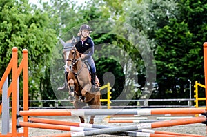 Young girl participating in a show jumping competition with her mare