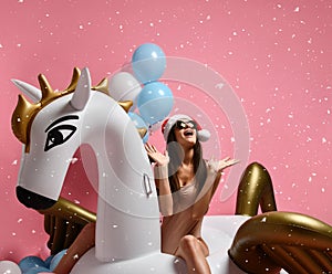 Young girl with pastel air balloons on birthday holiday party having fun celebrating with unicorn pegasus float in Santa hat