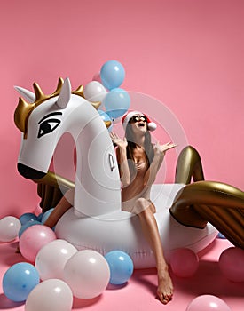 Young girl with pastel air balloons on birthday holiday party having fun celebrating with unicorn pegasus float in Santa hat