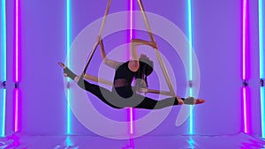 Young girl performs twine in the air, demonstrating exercises on aerial silk. Circus performer in black leotard against