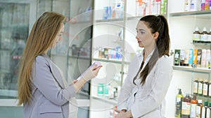 Young girl pharmacist advises pregnant customer. Pharmaceutical store concept