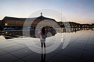 young girl photographing the Place de la Bourse and its reflection in a water mirror in Bordeaux in France