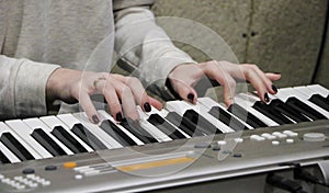 A young girl pianist plays the electronic piano with her favorite music. Female graceful hands touch the keys of the synthesizer c