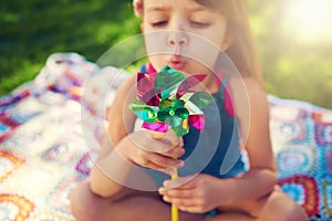 Young girl, picnic and blowing pinwheel, garden and enjoying freedom of outside and happy. Colourful little child