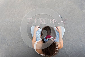 Young girl with pigtail sitting on the floor, paints a brooding reflexion with colored chalks on the asp