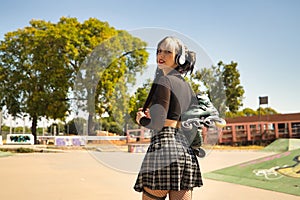 Young girl with pigtails, punk style, white headphones and inline skates hanging from the shoulder on their backs looking at