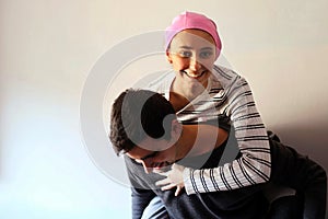 Young girl with pink handkerchief on her head on top of her husband. Concept of breast cancer patients photo