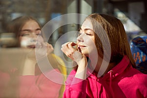 Young girl in pink hoodie sitting in public transport, modern tram, looking in window and smiling. Sunny day trip