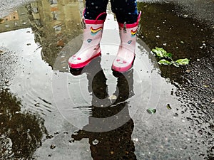 Young girl in pink  rubber boots standing in a puddle after a rain outdoor on spring day