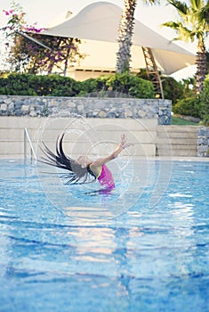 Young girl with pink swimsuit emerge from swimming pool, splash her hair