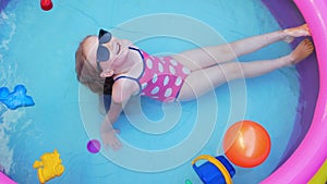 Young girl in pink swimsuit laughing playing in colorful inflatable swimming pool on a backyard. Summer domestic active lifestyle