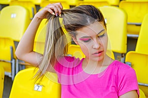 Young girl in a pink t-shirt sits on an empty tribune of the stadium