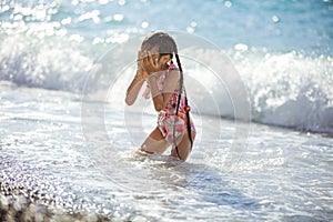 Young girl playing on beach in breaking waves and drying her face