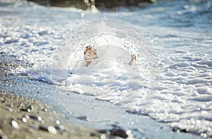 Young girl playing in breaking waves on beach. Big wave covering girl playing on sand