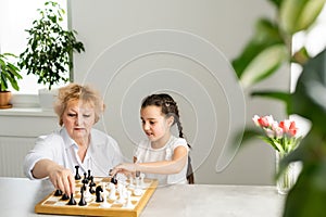 Young girl playing chess with grandmother together at home