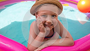 Young girl playing in colorful rainbow inflatable swimming pool.Child in straw hat and pink swimsuit in clear blue water.