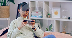 Young girl playing mobile games on a phone at home. A beautiful casual teenager feeling happy and relaxed, sitting on