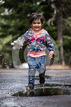 A young girl is playing in the rain, holding a stuffed animal