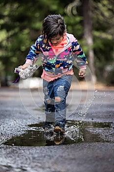 A young girl is playing in the rain, holding a stuffed animal