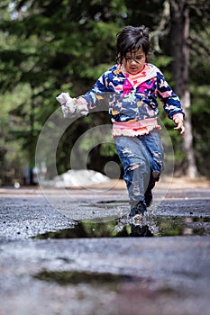 A young girl is playing in the rain, splashing in puddles