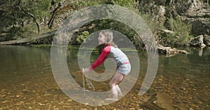 Young girl playing in a river flicks water into an arch and splashes ankle deep