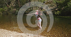 Young girl playing in a river flicks water into an arch and splashes ankle deep then walks out