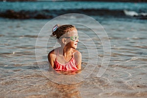 Young girl playing, swiming and splashing in fresh sea water. Smilling blonde girl in swimsuit with and swimming goggles