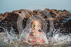 Young girl playing, swiming and splashing in fresh sea water. Smilling blonde girl in swimsuit with and swimming goggles