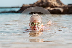 Young girl playing, swiming and splashing in fresh sea water. Smilling blonde girl in swimsuit with and swimming goggles