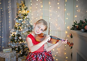 Young girl playing violin in front of christmas tree.