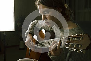 A young girl plays a sad melody on the guitar.