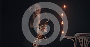 A young girl plays the saxophone on stage in a haze against a black background. There is inactive lighting in the background