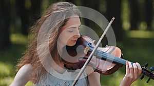 A young girl plays the violin in the city park.