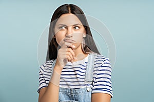 Young girl pondered, holding chin looking for solution coming up with idea thinks reflects analyzes