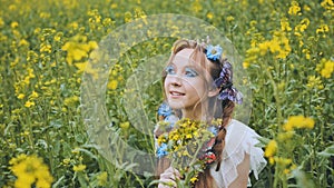 A young girl poses in a rapeseed field with a beautiful hairdo of flowers and butterflies.