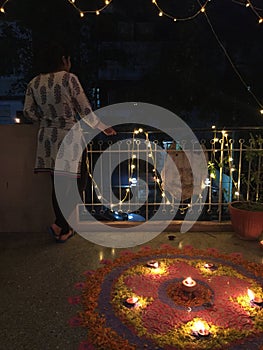 A young girl standing besides a brightly lit Rangoli during Diwali photo
