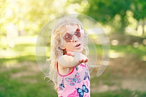 Young girl posing in fancy pink pentagonal shaped sunglasses outdoors. Cute adorable stylish Caucasian child with long blonde hair