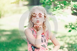 Young girl posing in fancy pink pentagonal shaped sunglasses outdoors. Cute adorable stylish Caucasian child with long blonde hair