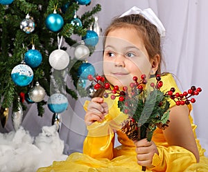 Young girl posing in front of christmas tree with decorations in her hands