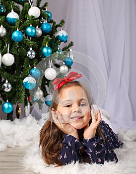 Young girl posing in front of christmas tree with red bow hair